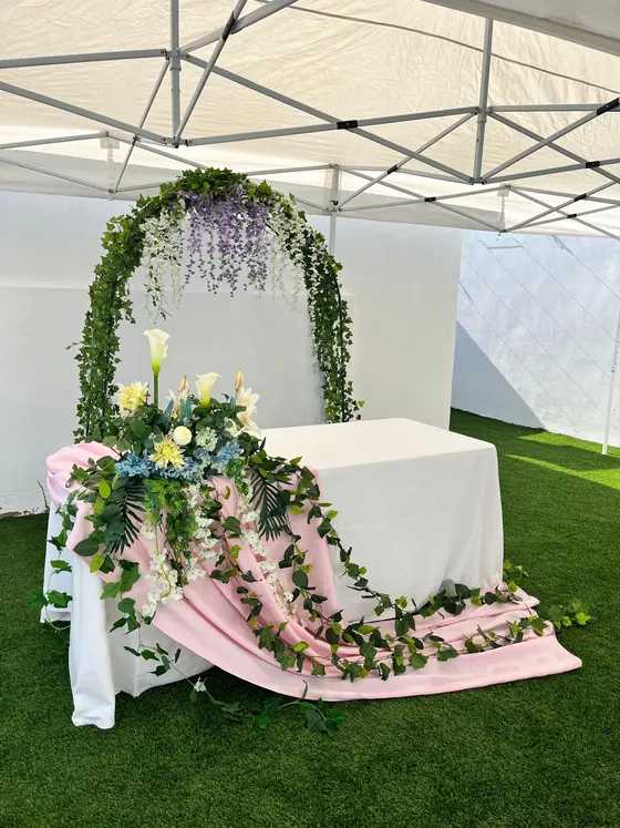 Altar de ceremonia con arco de hiedra y glicinias y mesa con flores sobre tela rosa, boda en Valencia