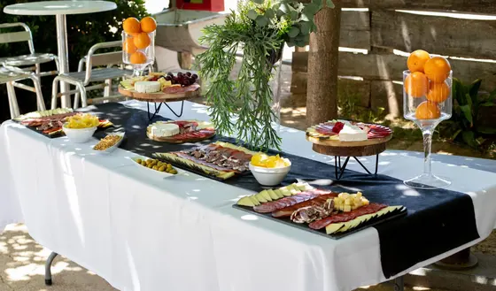 Mesa exterior con tablas de quesos y embutidos, naranjas y flores para una celebración al aire libre