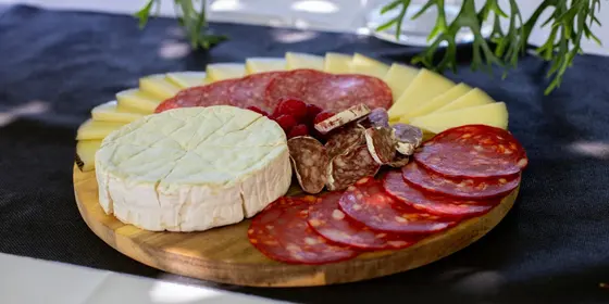 Tabla de quesos curados, brie, salchichón y frambuesas sobre madera